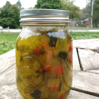 A mason jar of homemade zucchini relish on a wooden table outside.