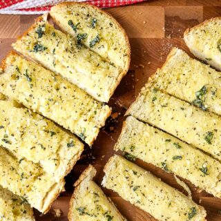 Homemade garlic bread cut into strips on a wooden cutting board.