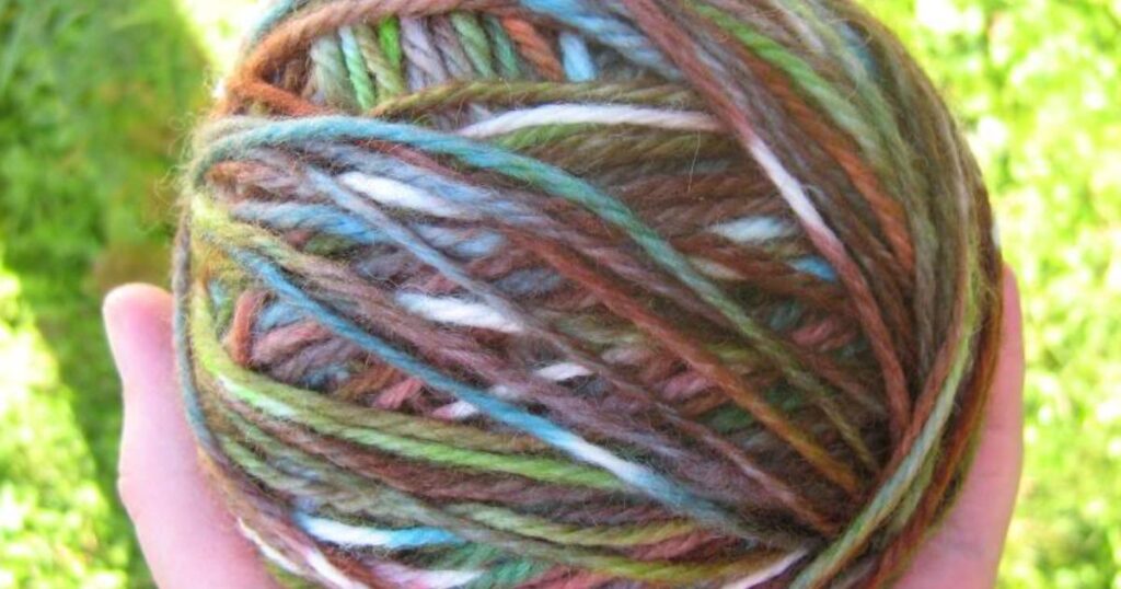 A hand holding a ball of home dyed yarn.