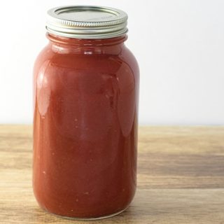 Homemade tomato sauce in a quart canning jar sitting on a wooden table.