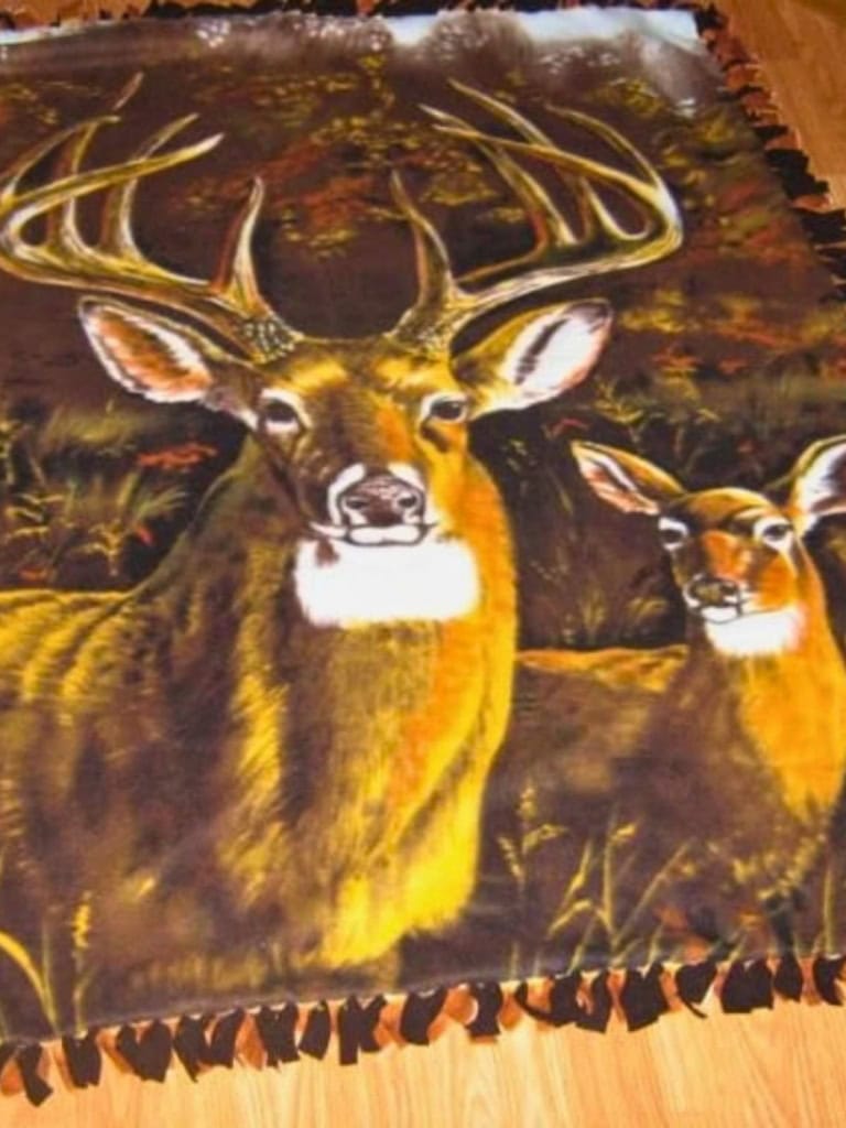 Finished no sew fleece blanket made with deer print fabric showing a large buck and a doe in a wooded scene. The blanket has knotted fringe around the edges created by tying strips of fleece together.
