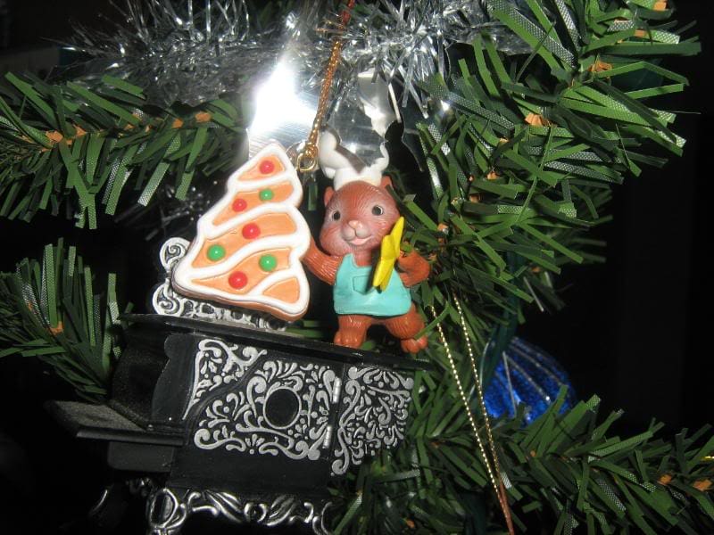 A wood stove Christmas ornament with a squirrel on top holding a cookie.