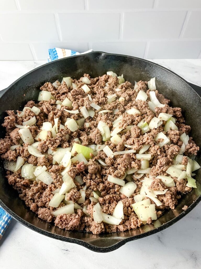 Adding diced onions and spices to the ground beef in the skillet.