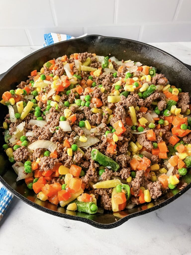 Skillet with ground beef, onions, frozen mixed vegetables.