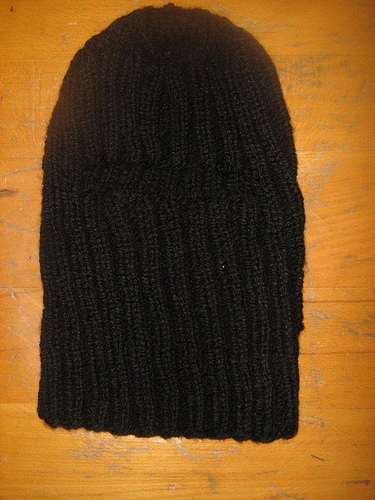 A homemade knit balaclava laying on a wooden table.