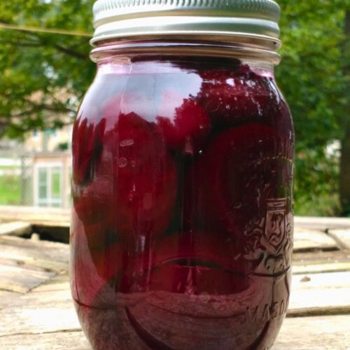 A jar of homemade pickled beets sits on a table outside.