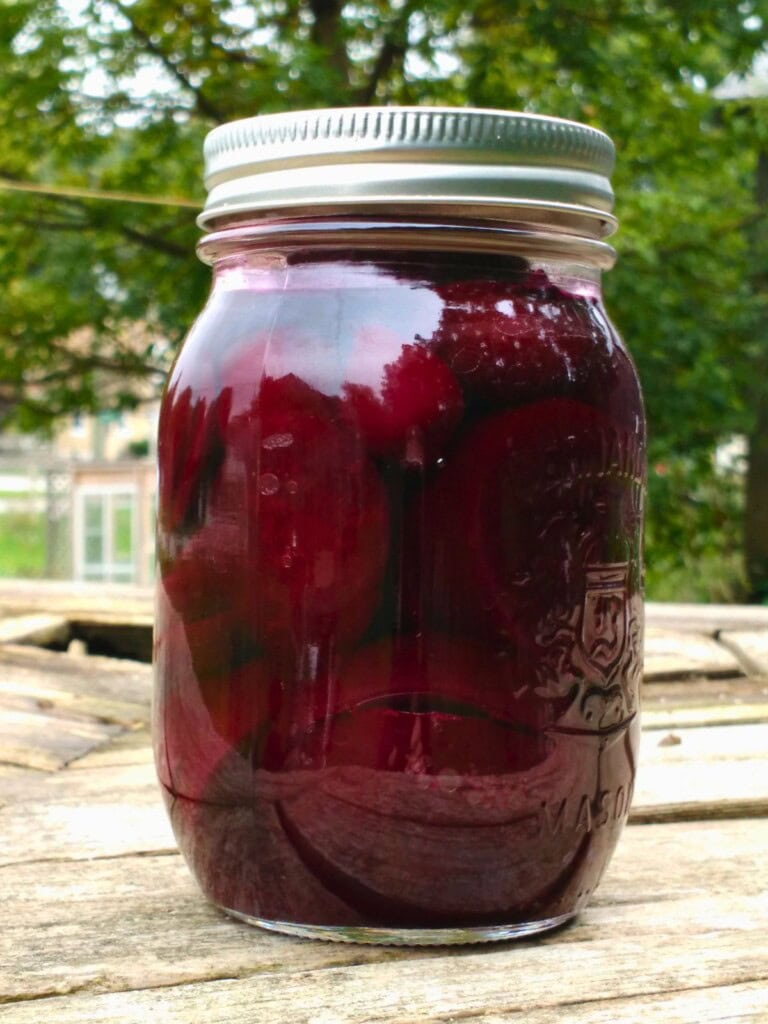 A jar of homemade pickled beets sits on a table outside.