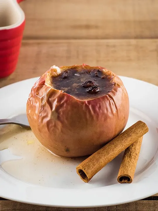 Baked apple filled with a sugar, cinnamon, and raisin mix on a white plate.