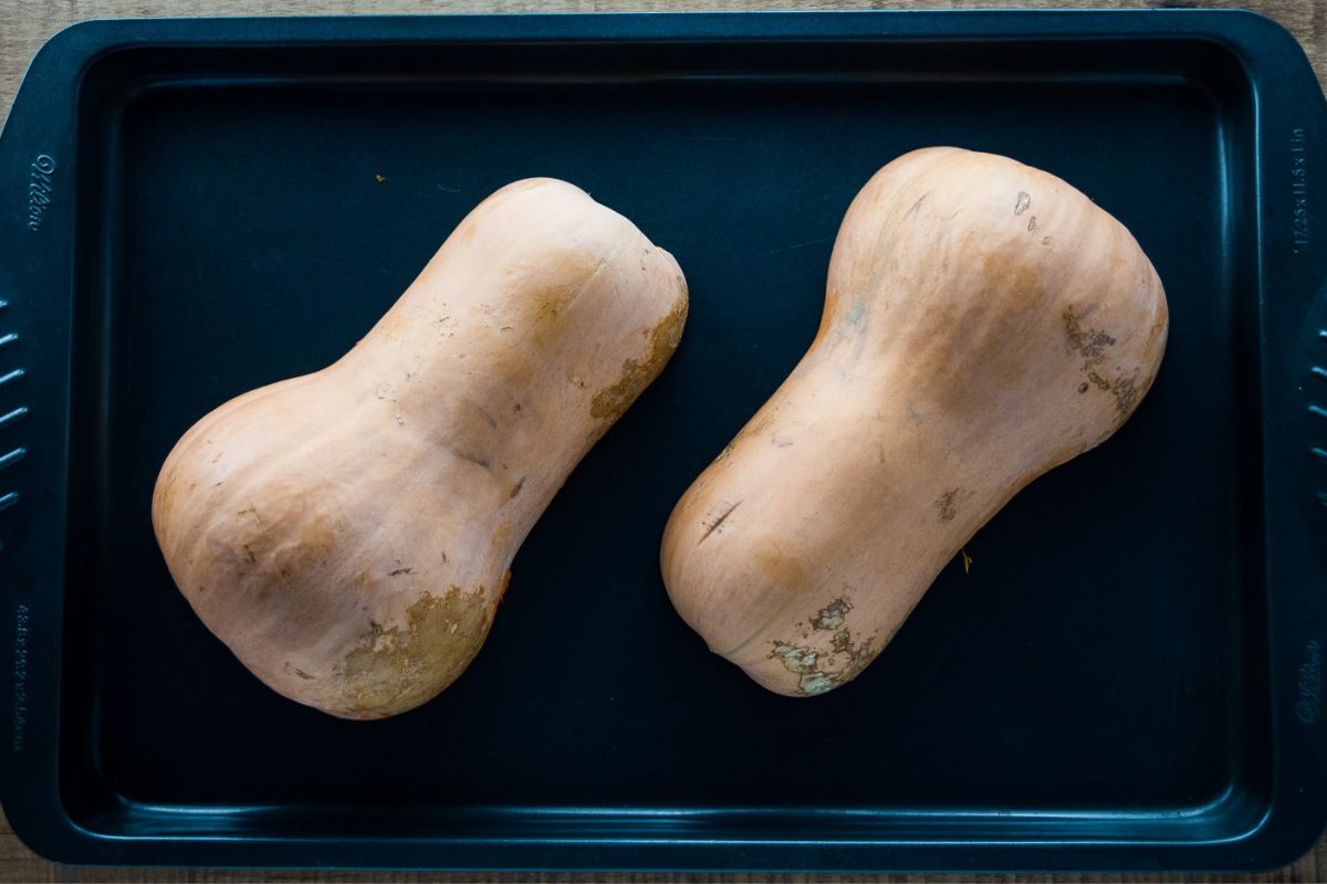 Butternut squash halves face down on a baking tray.
