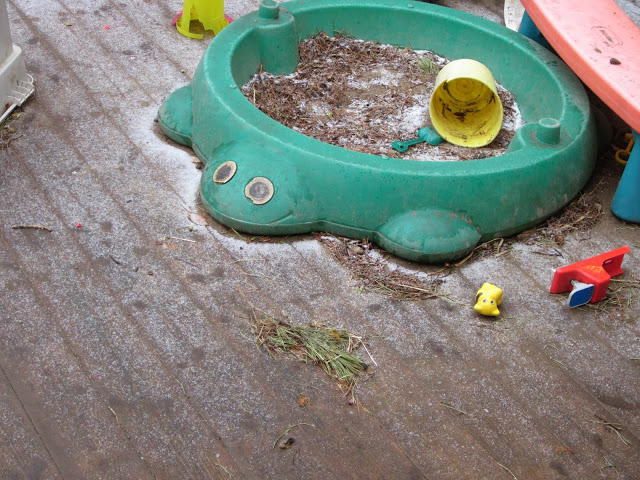 A turtle sandbox on a deck with a little snow around it.