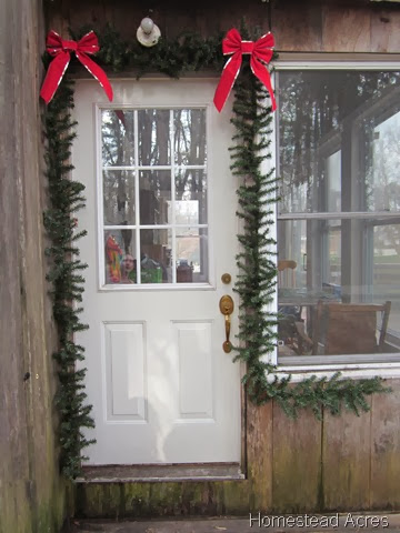Green garland hanging around a white front door with red ribbons on the corner.