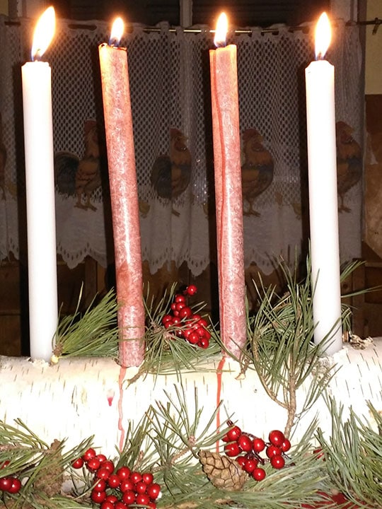 Homemade birch candle holder on a table with greenery around it and lit candles.