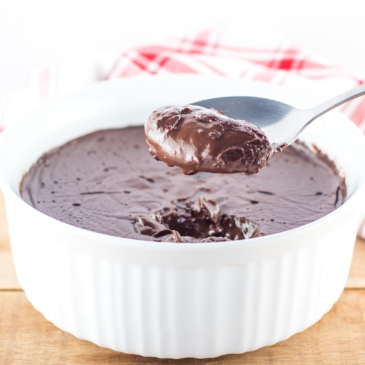 Homemade chocolate pudding in a white bowl with a spoonful being held up to eat.