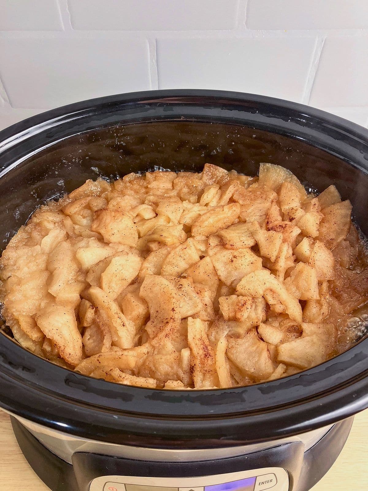Softened cinnamon apples cooking down in a black slow cooker with juices bubbling around the edges. This stage of the slow cooker apple butter recipe shows the apples tender and ready to be blended smooth.