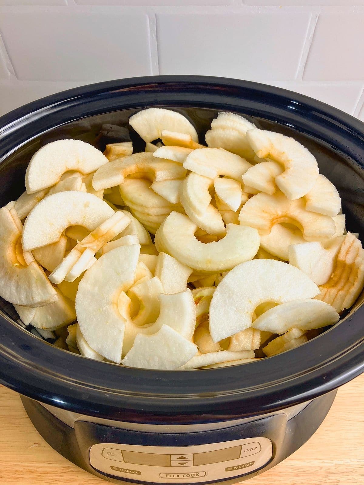 Peeled and sliced apples piled inside a black slow cooker before cooking.