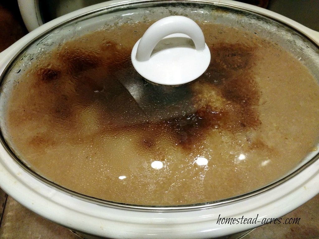 Slow cooker filled with pear sauce and spices with the lid on.