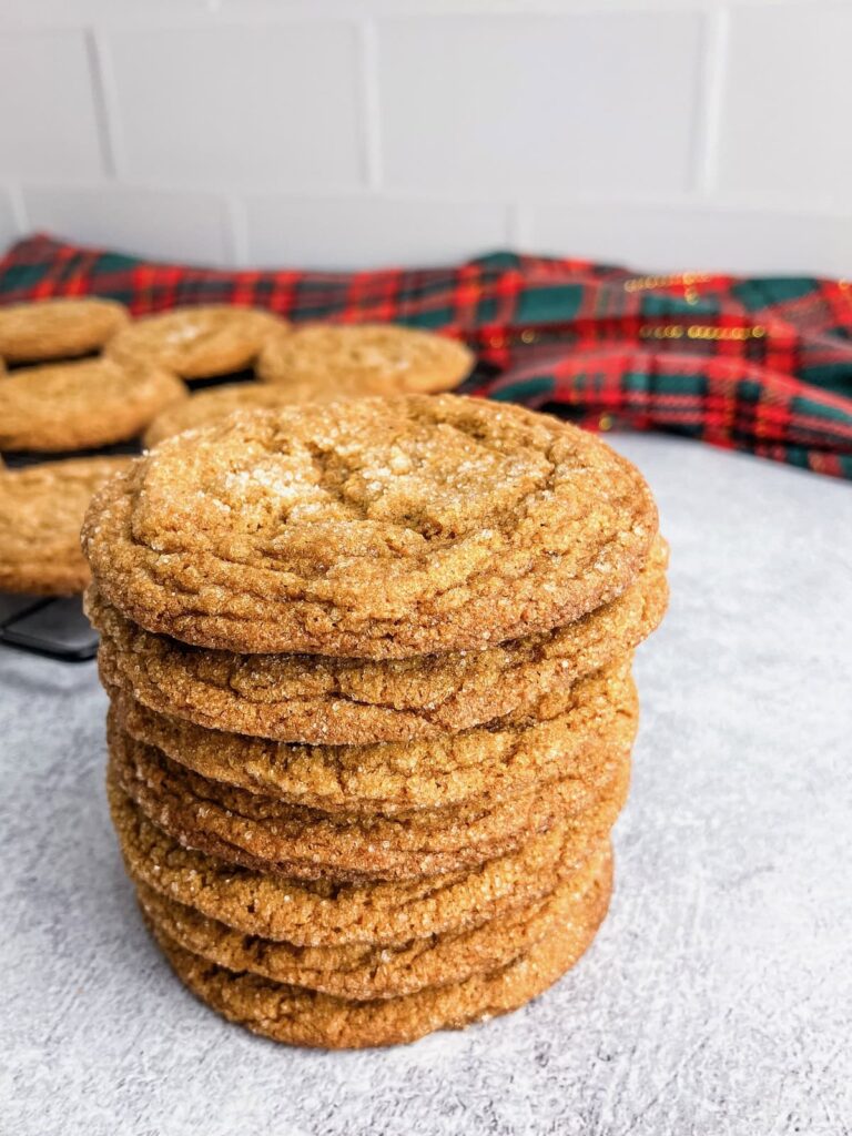 Chewy ginger molasses cookies stacked up in front of a cooling rack.