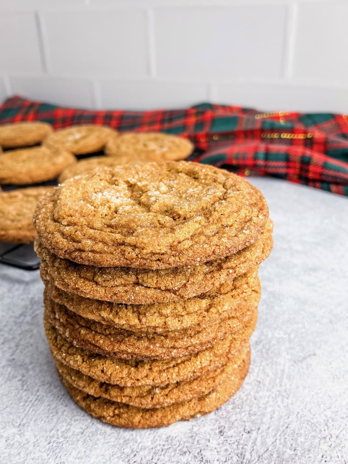 Chewy ginger molasses cookies stacked up in front of a cooling rack.