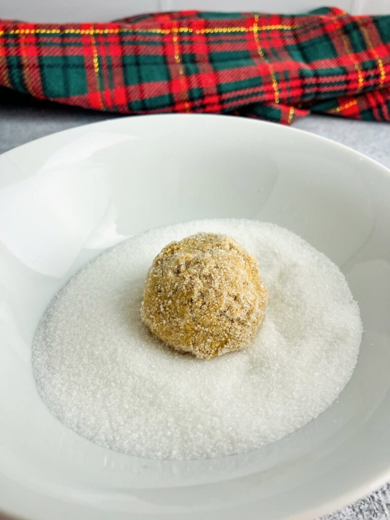 Ginger molasses cookie dough ball in a bowl of white sugar.