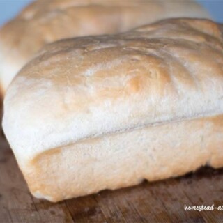 Two loaves of homemade white bread sitting on a cutting board.