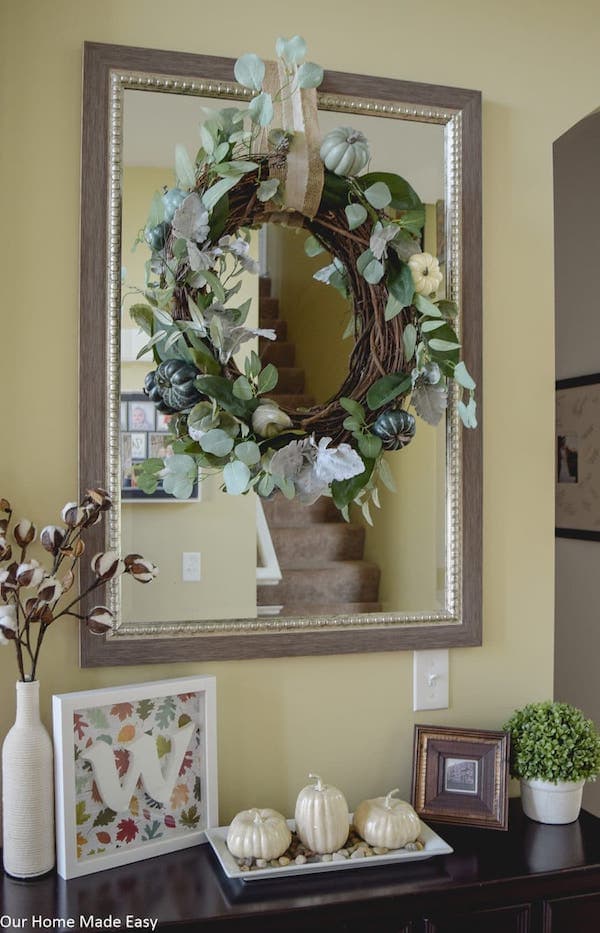 Homemade grapevine wreath with greens and green squash hanging over a mirror.
