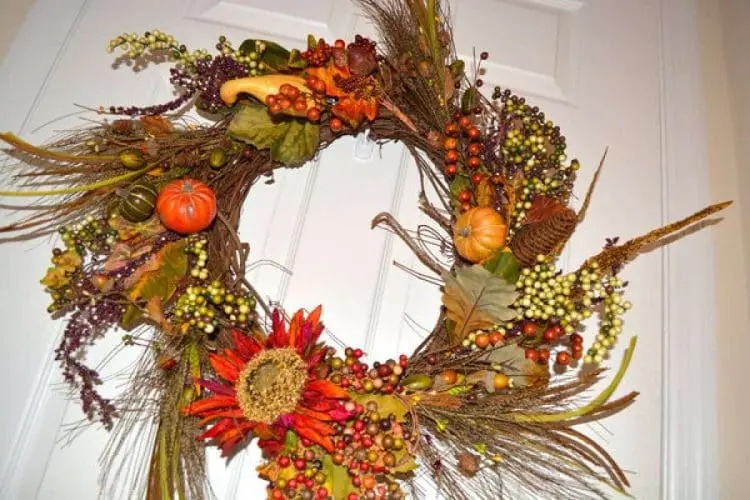 Grapevine wreath with dried flowers, grass, berries, and pumpkins hanging on a door.