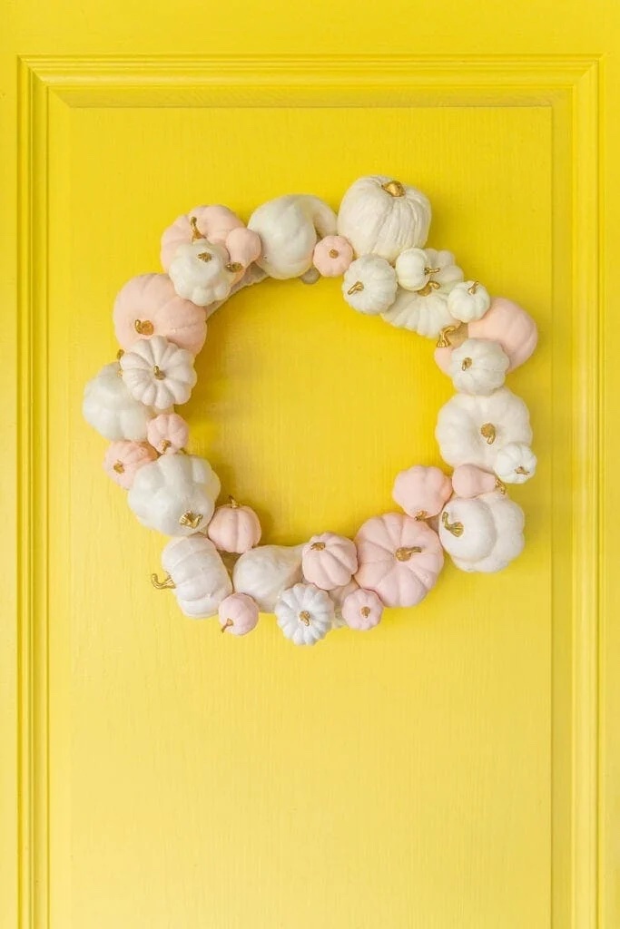 White and light pink pumpkin wreath hanging on a yellow door.