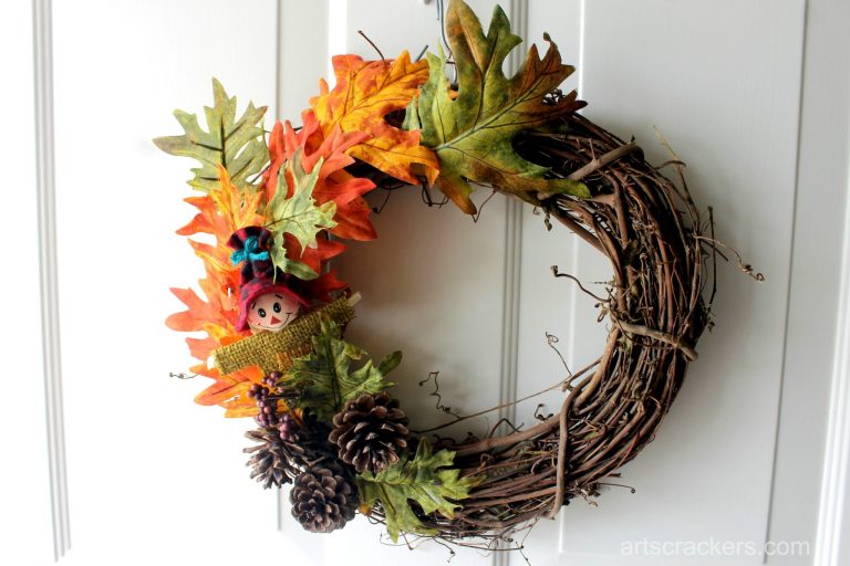 Grapevine wreath with a scarecrow face, pinecones, and leaves hanging on a white door.