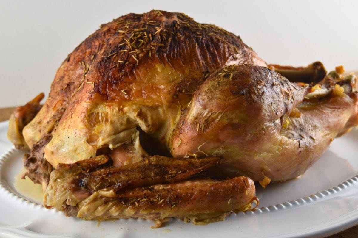 A roasted turkey on a white serving platter after cooking a moist turkey from frozen.