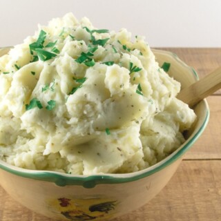 A yellow bowl filled with homemade garlic mashed potatoes and topped with fresh parsley.