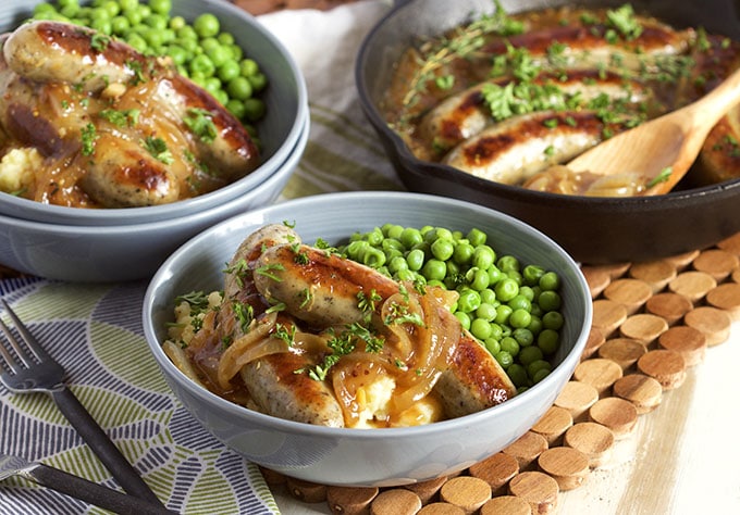 Bowls filled with mashed potatoes, sausage, peas, and caramelized onions.