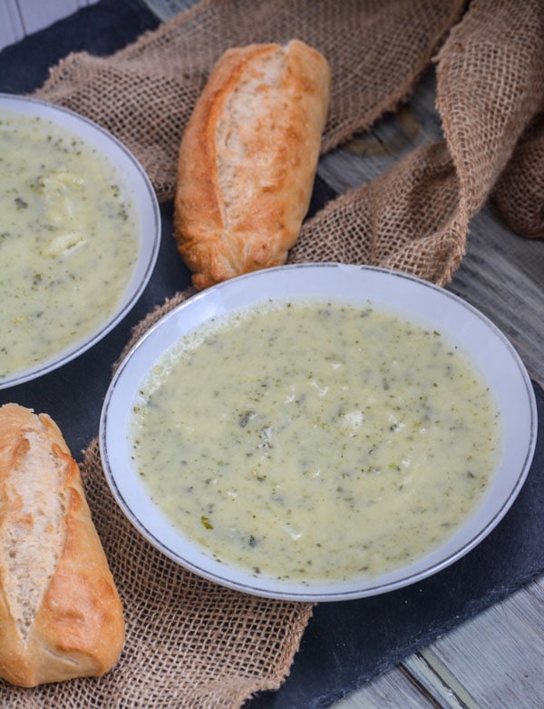 White bowls filled with Irish colcannon potato soup on a wooden table next to dinner rolls.