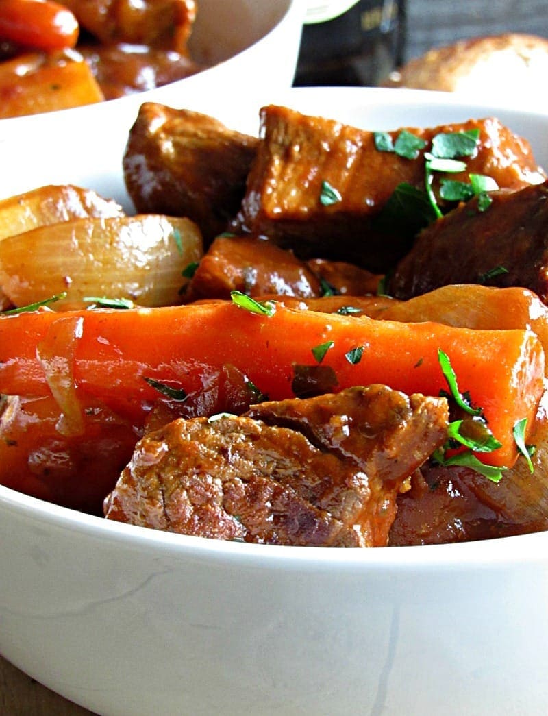 A white bowl filled with homemade Irish stew, chunks of carrot, onion, and meat.