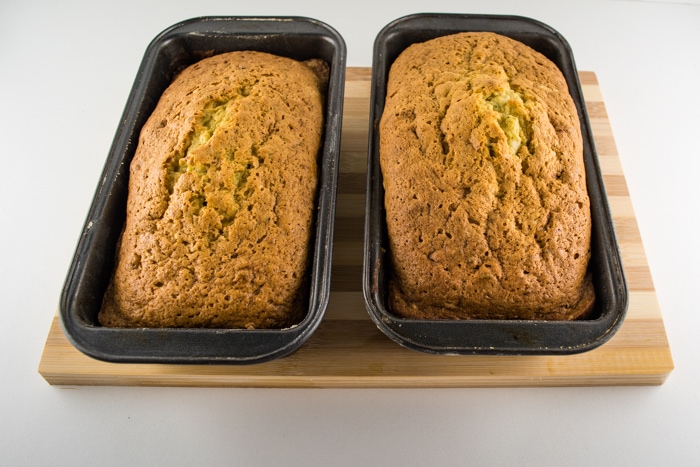 Warm zucchini bread cooling in pans sitting on a wooden cutting board.