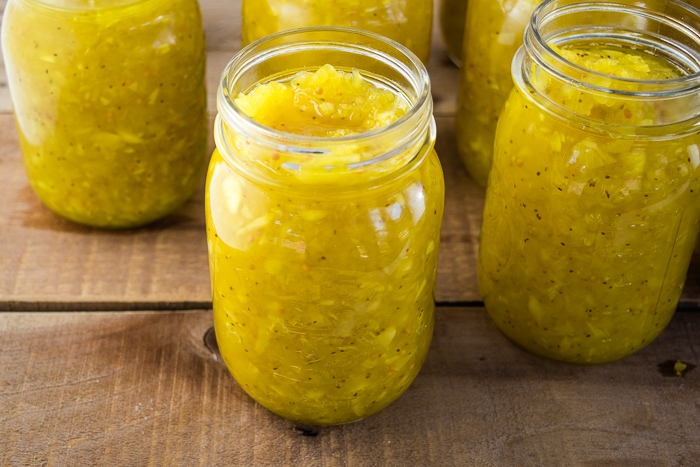 Canning jars filled with ripe cucumber relish sitting on a wooden table.