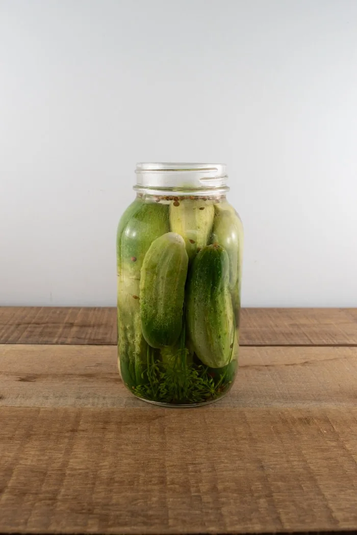 Jar filled with brine, spices, and cucumbers for homemade whole dill pickles.