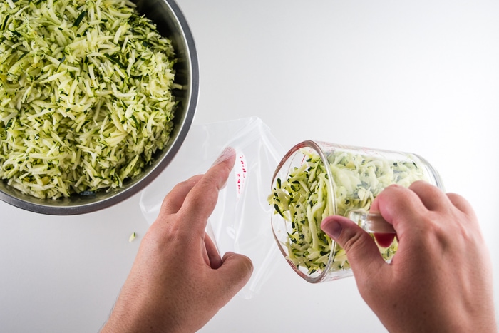 Measuring zucchini into serving sizes and pouring it into freezer bags.