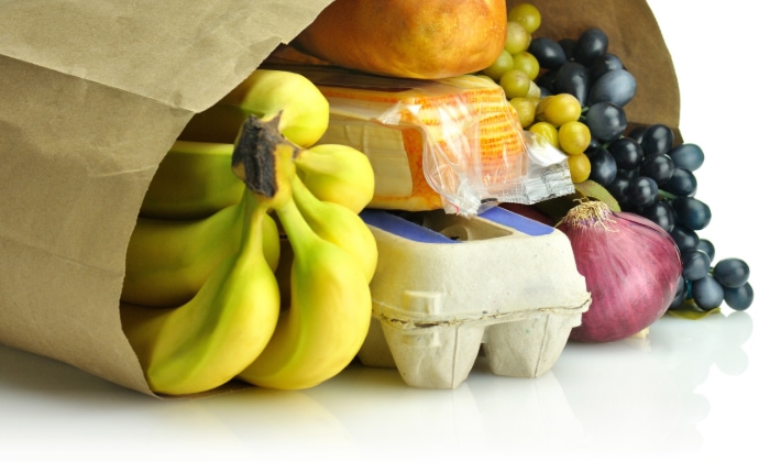 Shopping bag on a table filled with bananas, eggs, cheese, onions, and grapes.