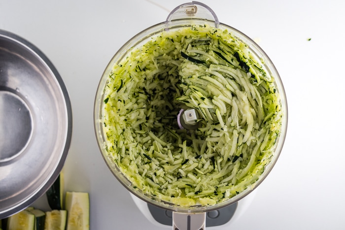 Shredding zucchini in a food processor bowl.
