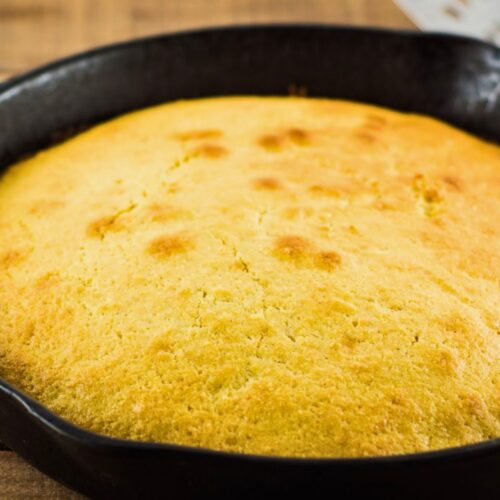 Golden skillet cornbread baked in a black cast iron pan with a lightly browned top and rustic texture. This skillet cornbread recipe without buttermilk is shown fresh from the oven and ready to serve.