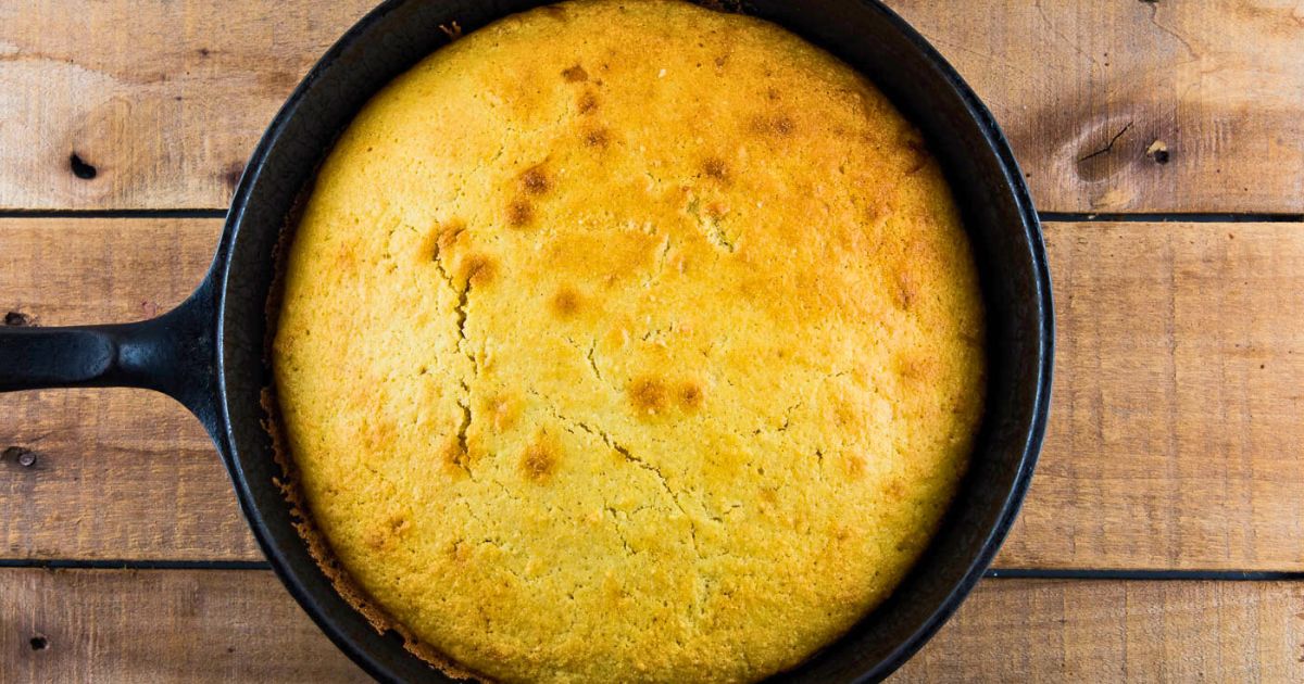 Warm homemade skillet cornbread in a cast iron skillet on a wooden table.