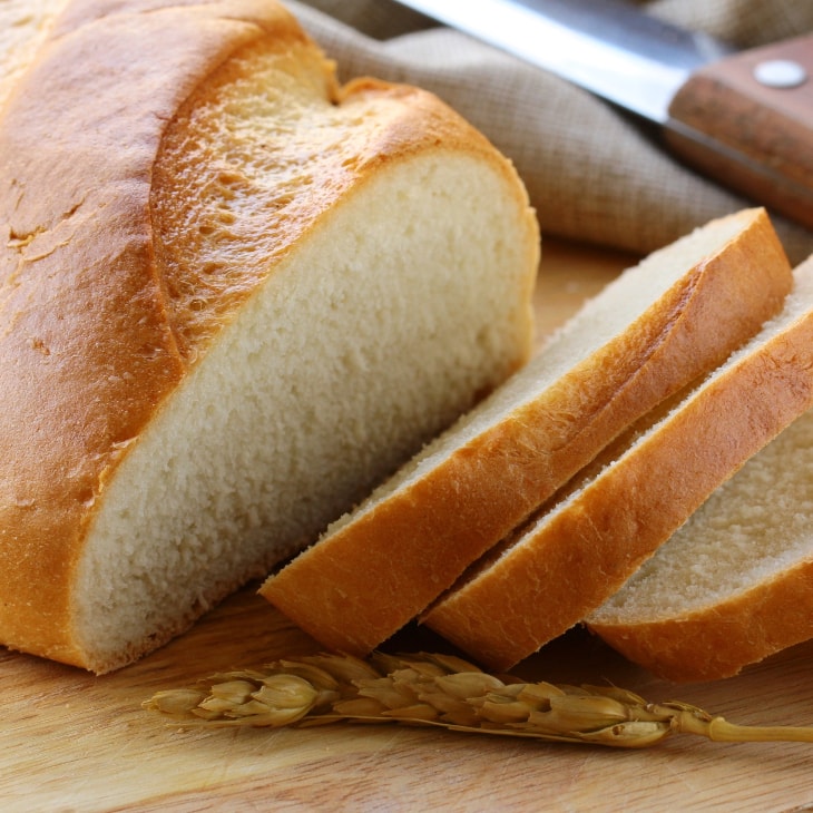 How To Freeze Bread - a loaf of fresh bread being sliced before freezing.