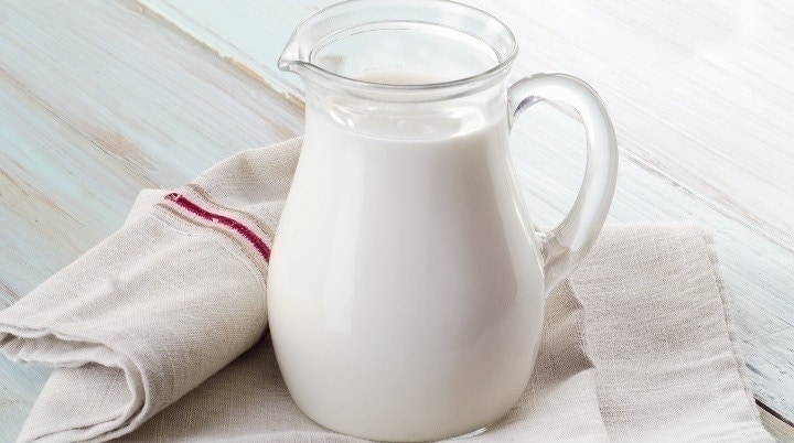 Milk jug filled with fresh thawed milk sitting on a wooden counter.