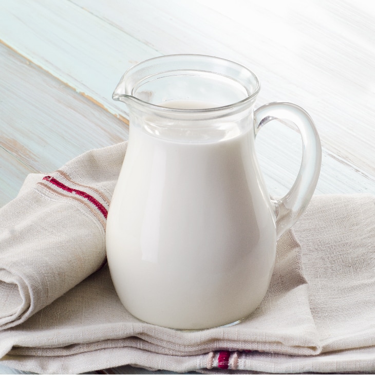 How To Freeze Milk - A glass jug filled with fresh milk sitting on a cream and white tea towel.