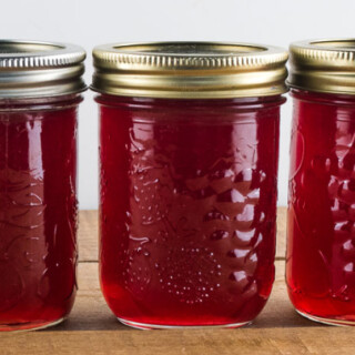 3 jars of red jelly sitting on a wooden table top