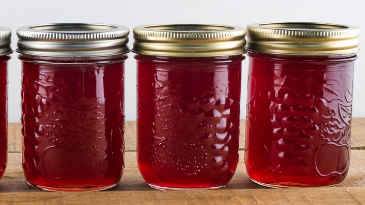 3 jars of red jelly sitting on a wooden table top
