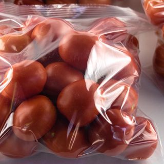 3 large bags of tomatoes on a table.