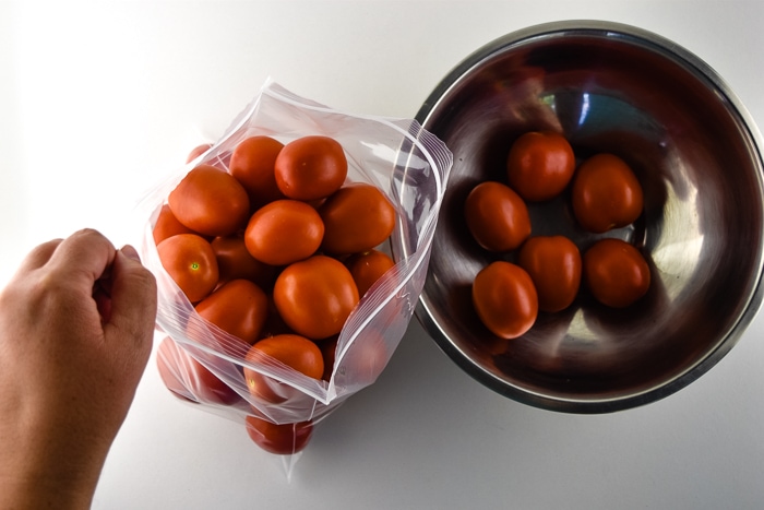Large bag full of tomatoes next to an almost empty bowl.