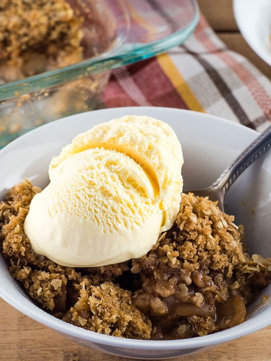 Homemade apple crisp served in a white bowl with ice cream on top.