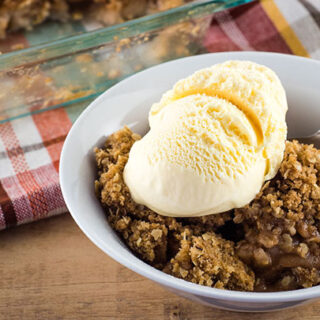 Warm homemade apple crisp served with ice cream in a white bowl.
